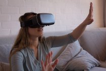 Женщина с гарнитурой виртуальной реальности на диване дома — стоковое фото