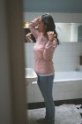Mujer de pie con la mano en el pelo en el baño en casa - foto de stock