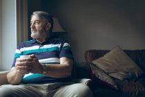 Thoughtful senior man looking through window at home — Stock Photo
