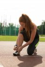 Jeune femme athlétique attacher lacets de chaussures sur une piste de course — Photo de stock