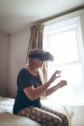 Пожилая женщина использует гарнитуру виртуальной реальности в спальне дома — стоковое фото
