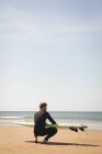 Surfista com prancha de surf sentado na praia em um dia ensolarado — Fotografia de Stock