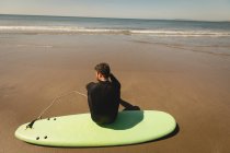 Vista posteriore del surfista seduto sulla tavola da surf in spiaggia — Foto stock