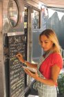Красива жіноча офіціантка пише меню на дошці меню під час використання цифрового планшета — стокове фото
