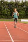 Jovem atlética feminina correndo em pista de esportes — Fotografia de Stock