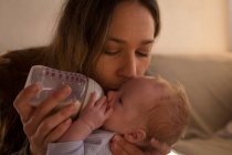 Primo piano della madre che bacia il suo bambino mentre alimenta il latte a casa — Foto stock
