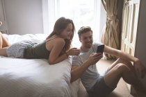 Couple utilisant un téléphone portable dans la chambre à coucher à la maison — Photo de stock