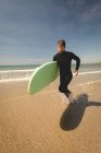 Surfeur avec planche de surf courir à la plage par une journée ensoleillée — Photo de stock