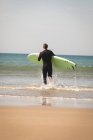 Rear view of surfer with surfboard running towards the beach — Stock Photo