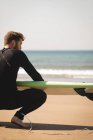Серфер с доской для серфинга, сидящий на пляже в солнечный день — стоковое фото