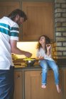 Отец взаимодействует со своей дочерью во время мытья овощей на кухне дома — стоковое фото