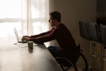 Инвалид использует ноутбук на обеденном столе дома — стоковое фото