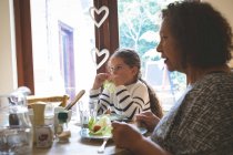 Großmutter und Enkelin essen zu Hause auf dem Esstisch — Stockfoto