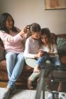 Tochter benutzt Handy, während Mutter sich zu Hause eine Frisur schneidet — Stockfoto