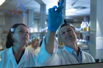 Équipe de scientifiques discutant sur panneau de verre en laboratoire — Photo de stock