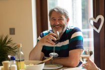 Uomo anziano con vino rosso sul tavolo da pranzo a casa — Foto stock
