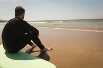 Surfer sitzt an einem sonnigen Tag auf einem Surfbrett am Strand — Stockfoto