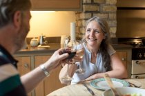 Senior pareja tostando copas de vino en casa - foto de stock