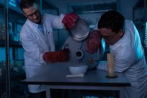 Científicos masculinos vertiendo líquido en un recipiente en el laboratorio - foto de stock
