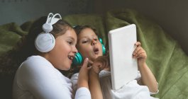 Hermanos escuchando música mientras usan tableta digital en casa - foto de stock