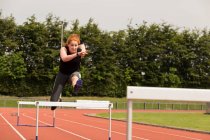 Female athletic jumping over hurdle on sports track — Stock Photo
