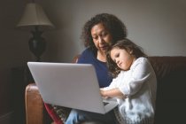 Kleines Mädchen benutzt Laptop mit Großmutter auf Sofa zu Hause — Stockfoto