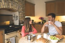 Casal interagindo uns com os outros enquanto toma café da manhã em casa — Fotografia de Stock