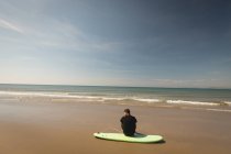 Rear view of surfer sitting on surfboard at beach — Stock Photo