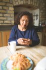 Старша жінка використовує мобільний телефон на кухні вдома — стокове фото