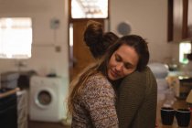 Pareja de lesbianas abrazándose en la cocina en casa - foto de stock