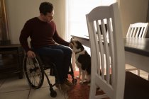 Людина з обмеженими можливостями погладжує собаку біля обіднього столу вдома — стокове фото
