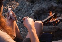 Close-up of man heating hot dog near campfire — Stock Photo