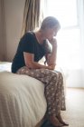 Worried senior woman sitting on bed in bedroom at home — Stock Photo
