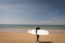 Surfer mit Surfbrett steht an einem sonnigen Tag am Strand — Stockfoto