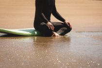 Низкая часть серфера, сидящего на доске для серфинга на пляже — стоковое фото