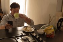 Человек, использующий мобильный телефон на обеденном столе дома — стоковое фото