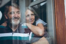 Happy senior couple looking through window at home — Stock Photo