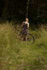 Вид ззаду жінки, що стоїть з велосипедом у полі — стокове фото