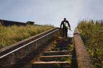 Low angle view of surfer with surfboard walking on staircase — Stock Photo