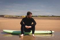Серфер, сидящий на доске для серфинга на пляже в солнечный день — стоковое фото