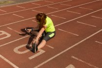 Mujer joven atlética usando el teléfono móvil mientras hace ejercicio en pista de atletismo - foto de stock