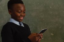 Schoolboy using mobile phone near chalkboard in classroom — Stock Photo