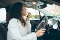 Seitenansicht einer Geschäftsfrau, die Lippenstift im Auto aufträgt — Stockfoto