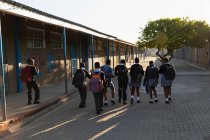 Colegiales caminando en el campus escolar en un día soleado - foto de stock