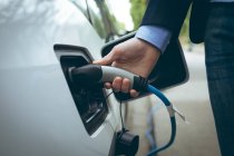 Gros plan de l'homme d'affaires rechargeant une voiture électrique à la station de recharge — Photo de stock