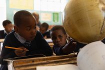 Школярки дивляться на глобус в класі в школі — стокове фото