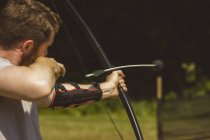 Hombre practicando tiro con arco en el campamento de entrenamiento en un día soleado - foto de stock