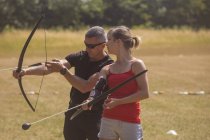 Entrenador instruyendo a la mujer sobre tiro con arco en el campo de entrenamiento - foto de stock