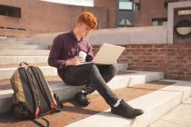 College student using laptop on stairs in college — Stock Photo