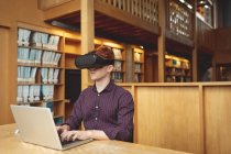Студент колледжа с помощью ноутбука и гарнитуры виртуальной реальности в библиотеке — стоковое фото